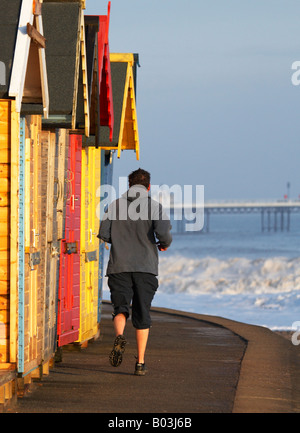 Jogger running along the seafront next to the brightly painted beach huts at Cromer seafront on the Norfolk Coast, UK. Stock Photo