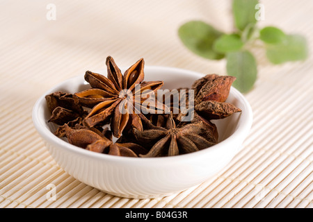 dried star anise in small white china bowl on straw mat, garnisched with leaves Stock Photo