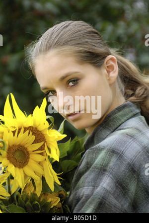 young natural woman with ponytail and karo shirt with a bunch of sunflowers in her arms Stock Photo