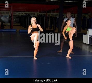 young female MMA fighters working on high knee kicks with their personal trainer in the gym Stock Photo