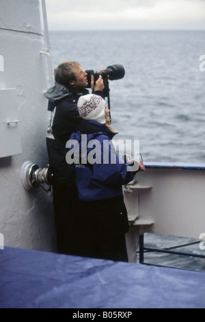 A photographer with an SLR and long telephoto lens with companion on board a boat at sea Stock Photo