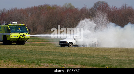 An airport firetruck sprays foam on two vehicles that were set on fire during a mock crash drill at Tweed New Haven Airport. Stock Photo
