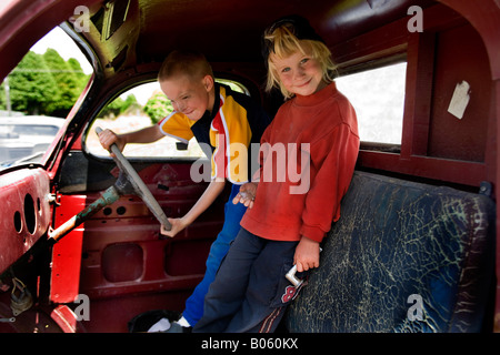 Two young boys playing in the front seats of a wrecked car Stock Photo
