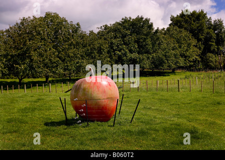 Large Apple sculpture in a orchard field surrounded by electric fence to protect it from cattle, New Zealand Stock Photo