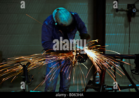 Male worker wearing appropriate safety equipment uses a grinder in the construction area of a piping fabrication plant Stock Photo