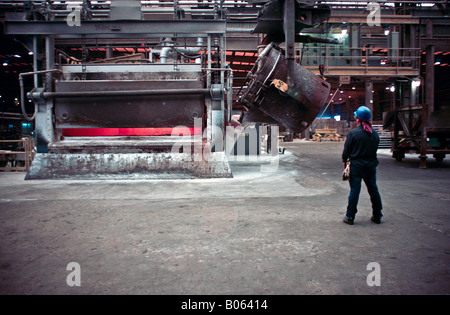 Primary aluminum reduction facility pot line with worker using radio to control the crane lifting crucible to pour molten metal Stock Photo