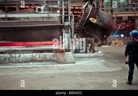 Primary aluminum reduction facility pot line with worker using radio to lift crane  crucible to pour molten metal Stock Photo