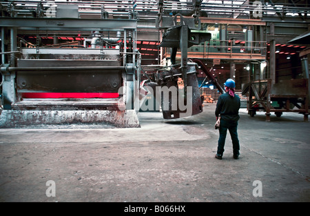 Primary aluminum reduction facility pot line with worker using radio to control the crane lifting crucible to pour molten metal Stock Photo
