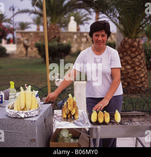 Lady preparing hot sweet corn cobs on barbecue in Platia Solomu Square at dusk Zakynthos Town Zakynthos Island The Greek Islands Stock Photo