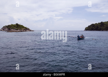 People wearing life jackets and snorkling equipment being towed with a rope behind a longtail boat Stock Photo