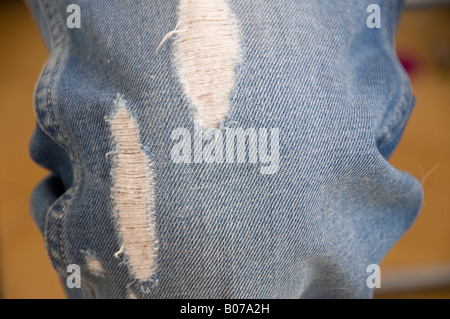 A close-up view of -blue ripped denim jeans featuring two distinct vertical rips or distressed patches, exposing the white horizontal threads Stock Photo