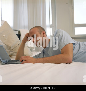 Young man in a Pajamas lying in bed next to a laptop Stock Photo