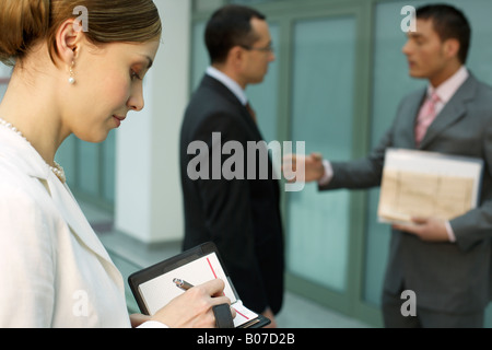 Two businessmen talking, in foreground businesswoman making notes Stock Photo