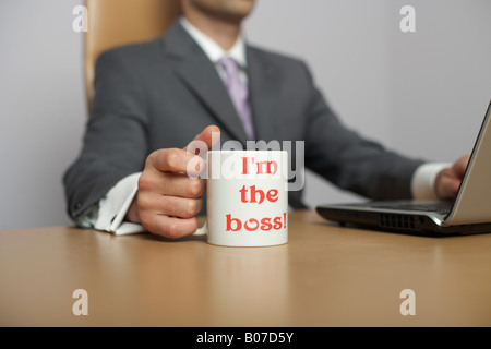 Businessman using laptop, I'm the boss! Coffee mug in foreground Stock Photo