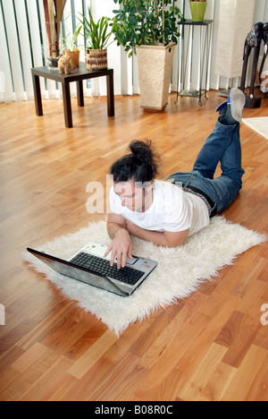 young man with laptop, lying on the floor in the living room Stock Photo