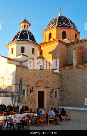 Tourists sitting at outside cafe tables in front of the two domes of the Iglesia de Nuestra Señora del Consuelo Church, Altea Stock Photo