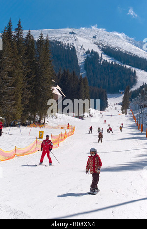 Child snowboarder and skiers coming down the Lukova ski slope in the Jasna Ski Resort, Lower Tatras, Slovakia Stock Photo