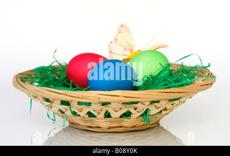 Pastel-coloured painted Easter eggs in basket with decorative butterfly Stock Photo