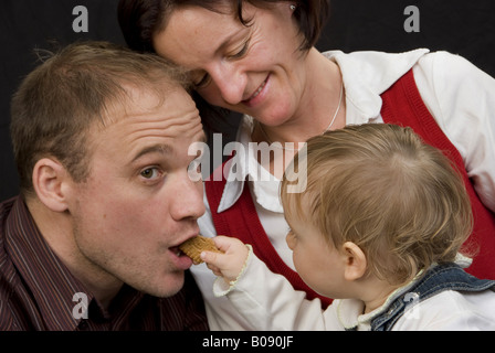 parents with daughter, child feeding his dad with a cookie Stock Photo