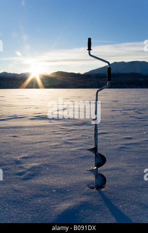 An ice fisherman using a hand auger to drill a hole on a frozen