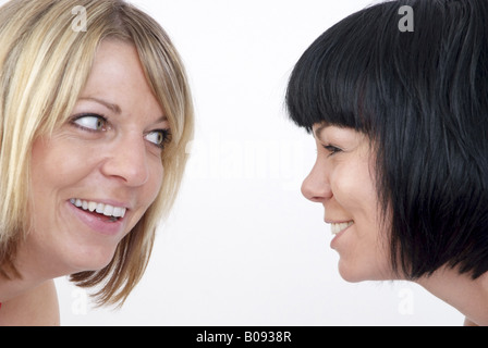 two laughing young women, one black-haired and one blond woman looking at each other Stock Photo