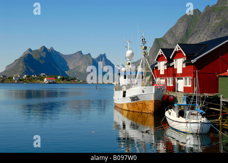 View of boats in the harbour, red wooden 'rorbu' houses, and mountains of Moskenesoya Island, Hamnøy, Reine, Lofoten Archipelag Stock Photo