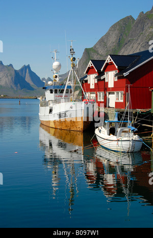 View of boats in the harbour, red wooden 'rorbu' houses, and mountains of Moskenesoya Island, Hamnøy, Reine, Lofoten Archipelag Stock Photo