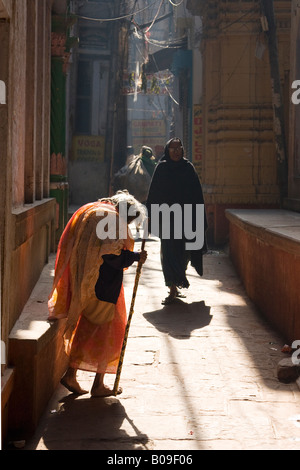 An old woman in an orange sari struggles to make her way up a street in the old town of Varanasi, india Stock Photo