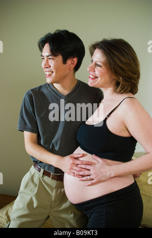 Young married couple Asian man and pregnant Caucasian woman posing together in their bedroom MODEL RELEASED Stock Photo