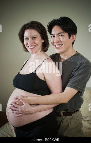 Young married couple Asian man and pregnant Caucasian woman posing together in their bedroom MODEL RELEASED Stock Photo