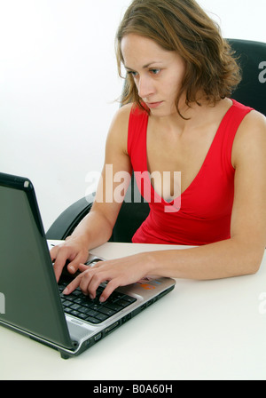 young woman in a red dress sitting in an office chair using a laptop Stock Photo