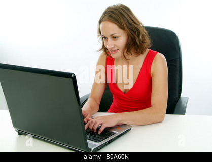 young woman in a red dress sitting in an office chair using a laptop Stock Photo