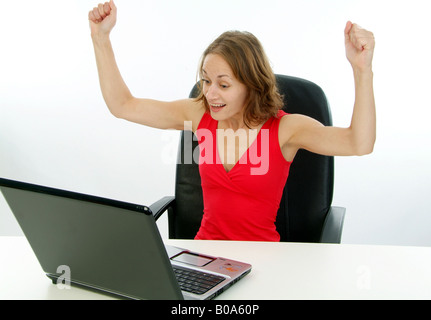 young cheering woman in a red dress working with a laptop Stock Photo