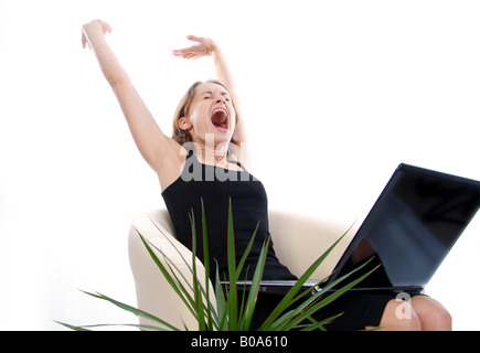 young woman with laptop sitting in an armchair, yawning and stretching out Stock Photo