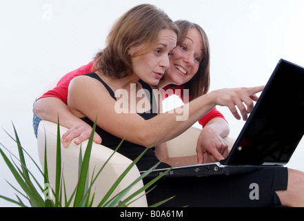 two cheerful young women using a laptop; one shows something on the screen to her girlfriend Stock Photo