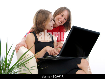 two cheerful young women using a laptop; one shows something on the screen to her girlfriend Stock Photo