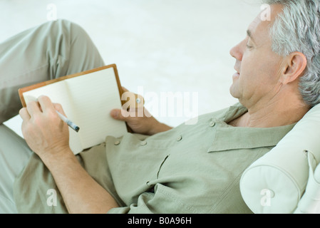 Mature man sitting, writing in diary, side view Stock Photo