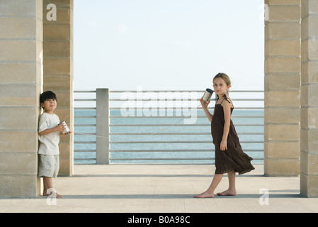 Two young friends playing with tin can phone together, girl looking at camera Stock Photo