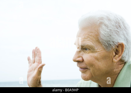 Senior man waving hand, smiling, side view Stock Photo
