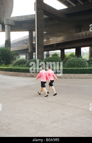 China, Guangzhou, two woman wearing matching uniforms walking under bridge, rear view Stock Photo