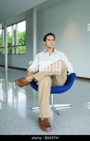 Young man sitting in chair, full length Stock Photo