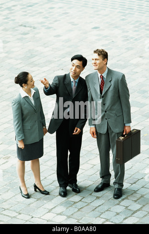 Three professionals standing together outdoors, one gesturing with hand, two looking up, high angle view Stock Photo