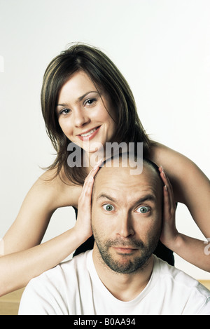 Woman covering man's ears with her hands, smiling, both looking at camera Stock Photo