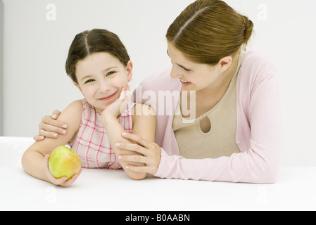 Woman and girl, girl holding apple, smiling at camera Stock Photo