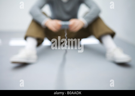Young man sitting on the ground, holding video game controller, cropped view, defocused Stock Photo