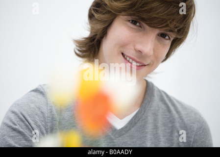 Young man holding flowers toward camera, smiling, close-up Stock Photo