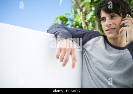 Young man leaning against wall, using cell phone Stock Photo