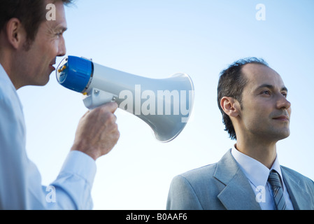 Businessman standing beside colleague, shouting into megaphone Stock Photo