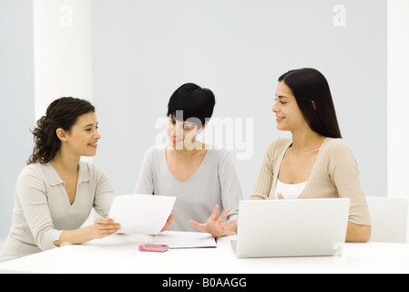 Three female professionals sitting at table, having discussion, one holding document Stock Photo