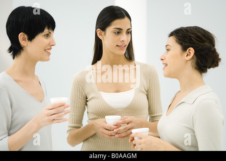 Three women chatting together, all holding disposable coffee cups Stock Photo